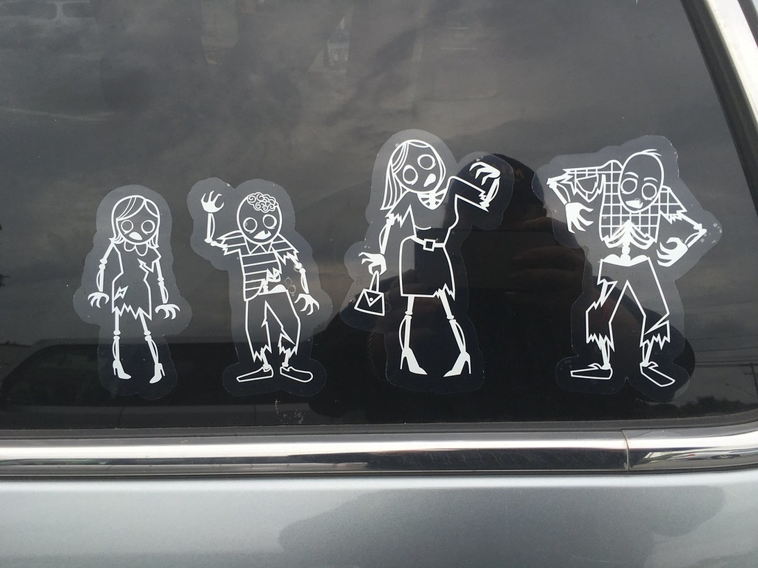 Närbild på en bils bakruta med vita dekaler som föreställer en zombiefamilj, ett kreativt sätt att dekorera familjebilen.