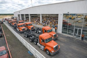 Orange begagnade lastbilar uppställda på rad vid en maskinauktion.